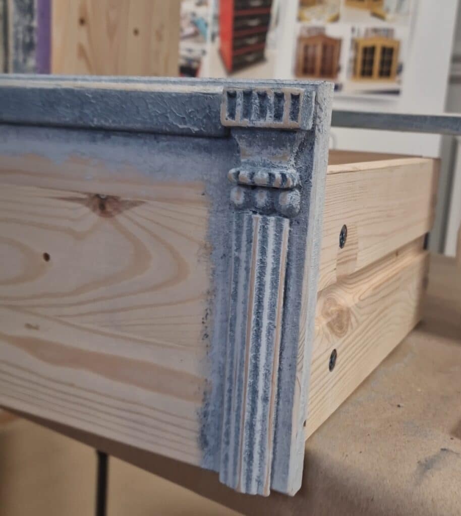 Zbliżenie na dekoracyjną listwę i rzeźbienia na froncie szuflady komody w stylu French Vintage, z efektem postarzania.