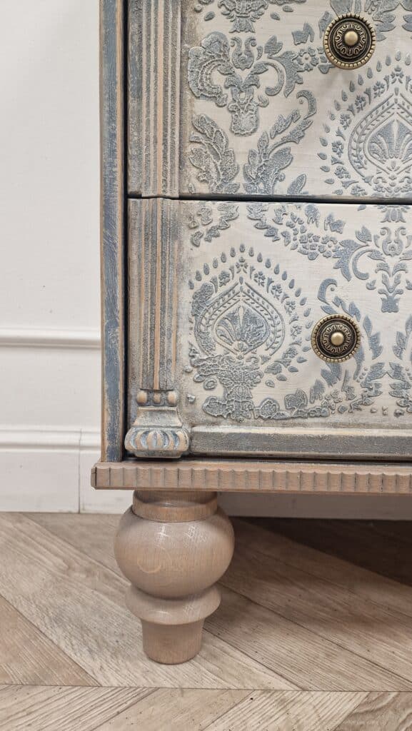 Zbliżenie na ozdobne fronty szuflad komody w stylu French Vintage, pokryte wzorzystą strukturą i przecieranym efektem.