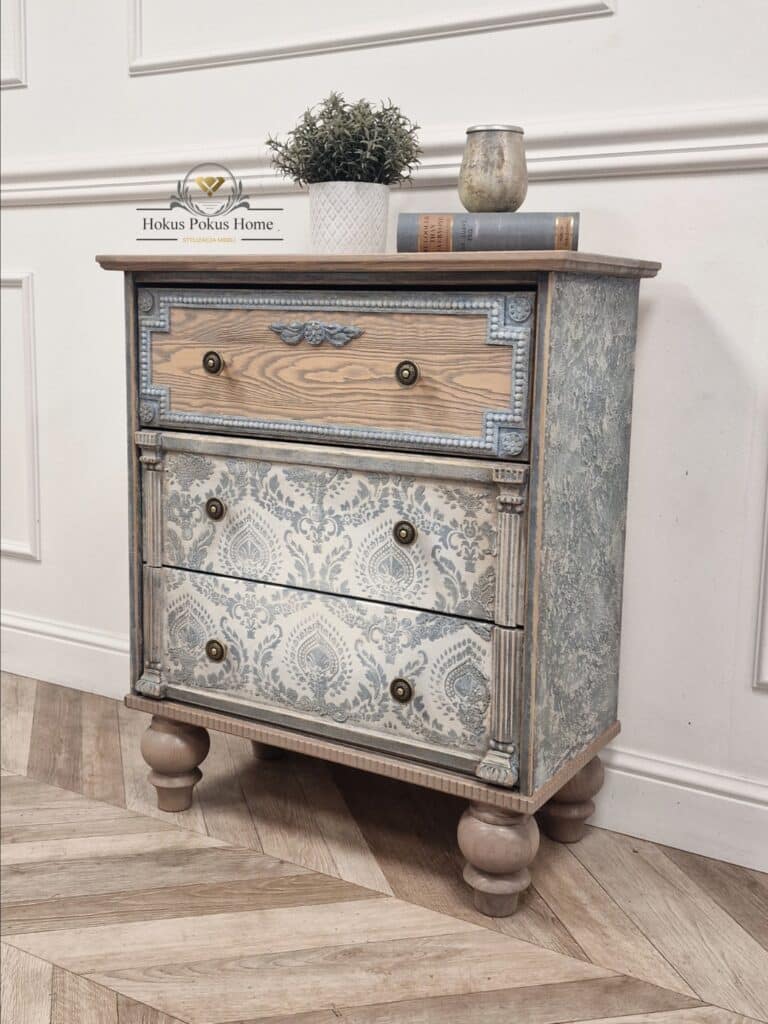 Stylizowana komoda French Vintage ustawiona w warsztacie stolarskim, ozdobiona książkami i doniczką z rośliną.