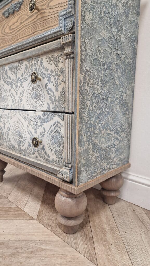 Komoda w stylu French Vintage z dekoracjami na blacie – książkami, doniczką i metalowym naczyniem.