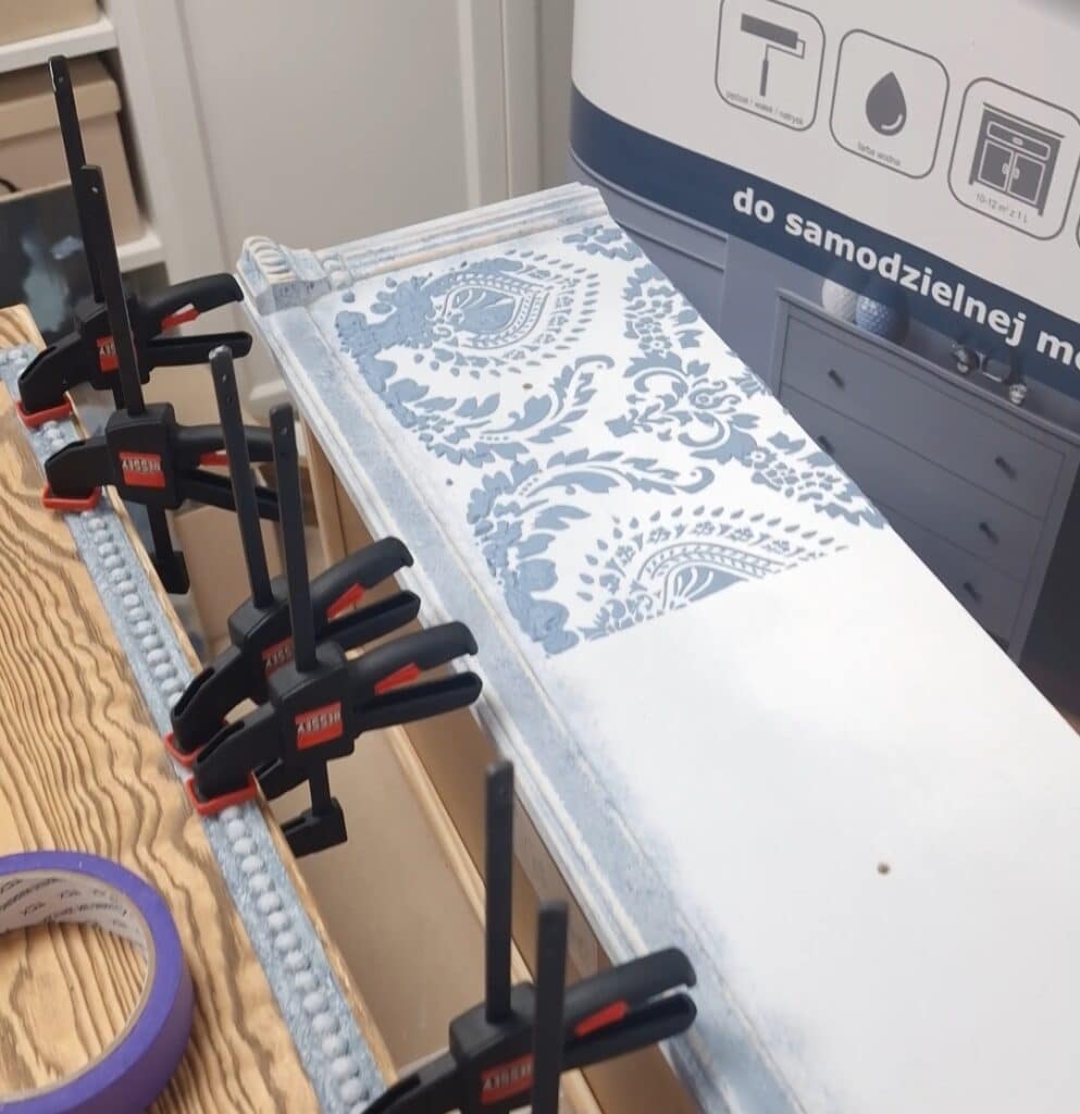 Front szuflady komody w stylu French Vintage w trakcie montażu, ozdobiony wzorzystą strukturą i przytwierdzany za pomocą ścisków stolarskich.